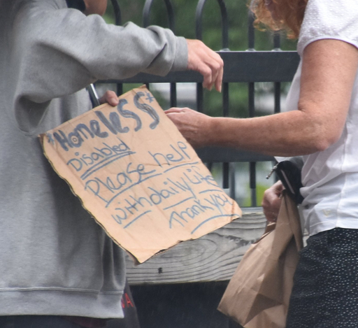 A panhandler gets a donation from a passer-by on the Whetstone Pathway in Brattleboro in this 2018 file photo.